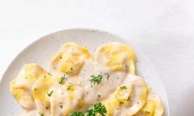 Teigtaschen mit einer cremigen hellen Soße auf einem weißen Teller