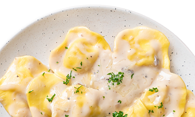 Italienische Teigtaschen in einer hellen cremigen Soße bestreut mit Petersilie auf einem weißen Teller