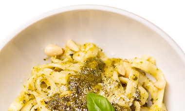 Nudeln mit grünem Pesto auf einem weißen Teller, dekoriert mit Pinienkernen